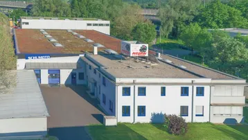 Luftaufnahme eines Gewerbegebäudes mit Flachdach und begrüntem Dachbereich, umgeben von Bäumen.
