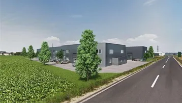 Moderne Gewerbeimmobilie mit dunkler Fassade und Parkplätzen, umgeben von grünen Feldern und einer Straße.