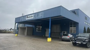 Außenansicht eines großen Industriegebäudes mit blauer Wellblechfassade und überdachtem Eingangsbereich.