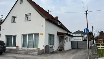 Weißes Einfamilienhaus mit Satteldach, großen Fenstern und einer Einfahrt.