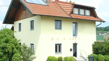 Traditionelles Einfamilienhaus mit gelber Fassade, Ziegeldach und Solarpaneelen auf dem Dach.