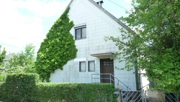 Einfamilienhaus mit bewachsener Fassade, umgeben von einem gepflegten Garten und Hecken.
