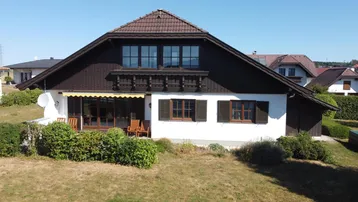 Charmantes Einfamilienhaus mit weißer Fassade, braunem Dach und einer gemütlichen Terrasse mit Gartenmöbeln.
