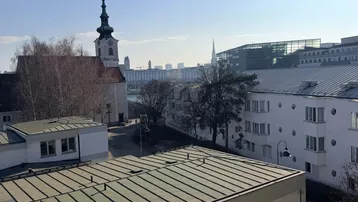 Panoramablick über die Stadt mit historischer Kirche und modernen Gebäuden unter blauem Himmel.