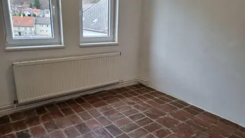 Heller Raum mit Terrakottafliesen, Heizkörper und Fenstern mit Blick auf grüne Hügel.