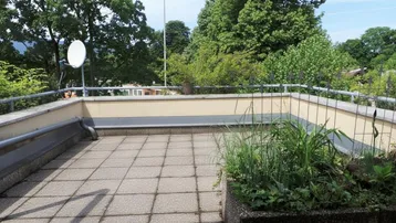 Geräumige Außenterrasse mit Fliesenboden, Pflanzenkübeln und einem weiten Blick ins Grüne.