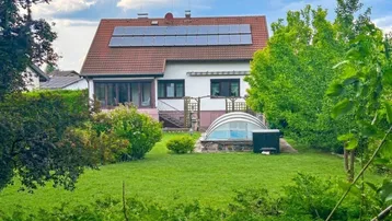 Großzügiger Gartenbereich mit Rasenfläche, Bäumen und einem überdachten Pool hinter dem Haus.