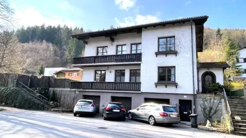 Traditionelles Wohnhaus mit mehreren Balkonen und Blick auf bewaldete Hügel.