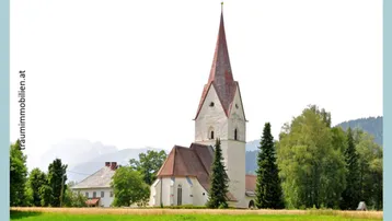 Malerische Kirche mit rotem Turm, umgeben von Bäumen und einer Bergkulisse.