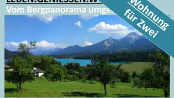 Malerischer Blick auf einen blauen See, umgeben von grünen Wiesen und majestätischen Bergen unter strahlendem Himmel.