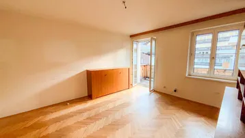 Helles Wohnzimmer mit Fischgrätparkettboden und Zugang zu einem Balkon.
