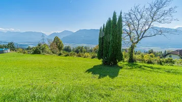 Weitläufige grüne Wiese mit Blick auf die umliegende Berglandschaft und einen See in der Ferne.
