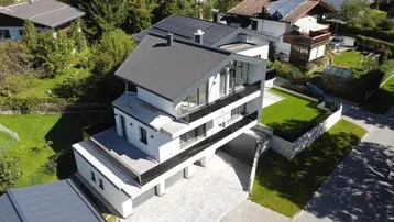 Moderne Architektur mit Flachdach und großen Glasflächen, umgeben von Grünflächen.