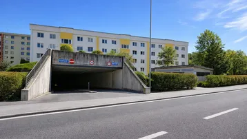 Eingang zur Tiefgarage eines Mehrfamilienhauses mit weiß-gelber Fassade unter blauem Himmel.