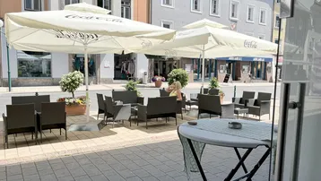 Gemütliche Außenterrasse mit Sonnenschirmen und Sitzgelegenheiten vor einer städtischen Kulisse.