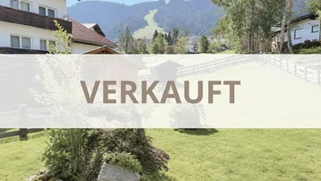 Blick auf ein traditionelles Gebäude mit Holzbalkon und die umliegende Berglandschaft mit Skipiste.