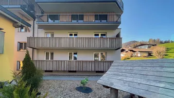 Modernes Mehrfamilienhaus mit Holzverkleidung und Balkonen, umgeben von einer kleinen Grünfläche.