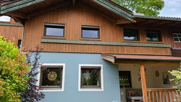 Seitenansicht des Hauses mit blauer Fassade, Holzverkleidung und überdachtem Außenbereich.