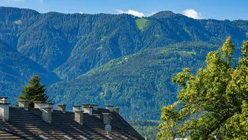 Panoramablick auf die bewaldeten Berge und die Dächer der umliegenden Gebäude unter blauem Himmel.