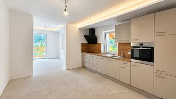 Moderne Einbauküche mit beigen Fronten und Holzakzenten, ausgestattet mit Backofen, in einem noch unfertigen Raum.