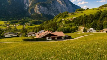 Weitläufige alpine Landschaft mit einem Haus in der Ferne, umgeben von grünen Wiesen und hohen Bergen.