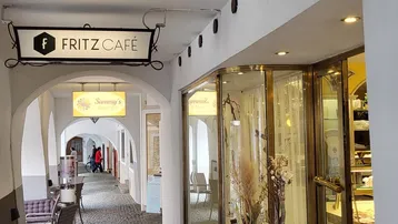 Historische Ladenpassage mit Arkaden und Außensitzplätzen, beleuchtet von Leuchtreklamen.