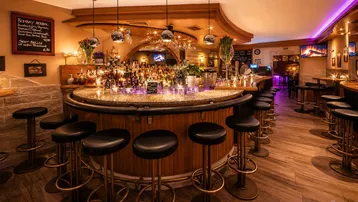 Eine elegant beleuchtete Bar mit einer großen, runden Theke, vielen Flaschen und bequemen Barhockern.