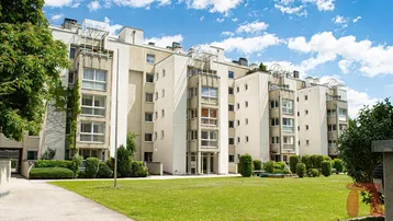 Modernes Mehrfamilienhaus mit gepflegter Grünanlage und blauer Himmel an einem sonnigen Tag.