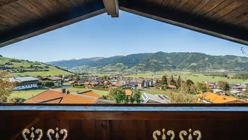 Panoramablick von einem traditionellen Holzbalkon auf ein malerisches Dorf und die umliegende Berglandschaft.