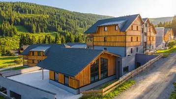 Mehrere moderne Gebäude mit Holzfassaden in alpiner Landschaft und grünen Bergen.