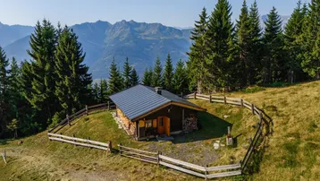 Charmante Holzhütte in alpiner Landschaft mit umlaufendem Zaun und Bergblick.