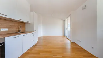 Heller offener Wohnbereich mit integrierter Küche, Holzboden und Zugang zu einem Balkon.