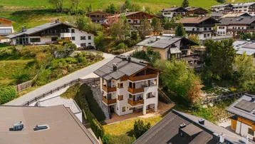 Luftaufnahme eines mehrstöckigen Gebäudes in einer bergigen Wohngegend mit traditioneller Architektur.