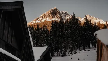 Majestätischer Berggipfel in der Abendsonne, umgeben von dichtem Nadelwald und Schnee.