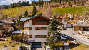 Großzügiges Haus in alpiner Landschaft mit grünen Hügeln und schneebedeckten Bergen im Hintergrund.