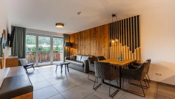 Moderner Wohn-Essbereich mit Holzwand, Fliesenboden und Zugang zu einem Balkon mit Bergblick.