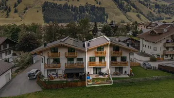 Luftaufnahme eines modernen Mehrfamilienhauses mit Balkonen und einer kleinen Terrasse, umgeben von grünen Hügeln.
