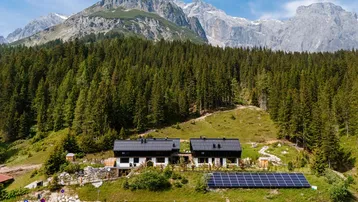 Zwei moderne Gebäude in alpiner Umgebung mit Photovoltaikanlage und Bergblick.