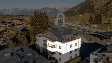 Luftaufnahme eines modernen Wohngebäudes in alpiner Landschaft mit Bergblick.