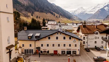 Malerisches Dorf in einem Tal mit traditionellen Gebäuden und schneebedeckten Bergen im Hintergrund.