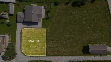Luftaufnahme eines Baugrundstücks von 554 m² in einer grünen Umgebung mit Bergblick.
