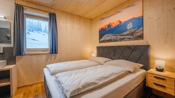 Gemütliches Schlafzimmer mit Holzwänden, Doppelbett und Blick auf die verschneite Berglandschaft.