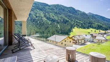 Geräumige Holzterrasse mit Liegestühlen und Bergblick, ideal zum Entspannen in der Sonne.