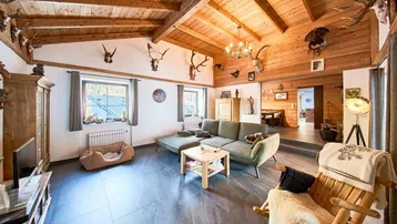 Geräumiges Wohnzimmer im alpinen Stil mit Holzbalkendecke, Kamin und traditioneller Hirschgeweih-Dekoration.