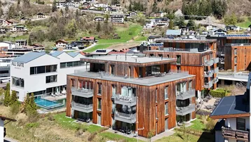 Moderne Gebäude mit Holzfassaden und Balkonen in einer grünen Berglandschaft.