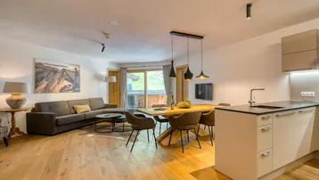 Geräumiger offener Wohn- und Essbereich mit moderner Küche, Holzboden und Zugang zum Balkon mit Bergblick.