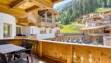 Großer Holzbalkon mit Sitzgelegenheiten und Panoramablick auf die umliegenden Berge und Chalets.