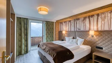 Gemütliches Schlafzimmer im alpinen Stil mit Holzelementen, Bergblick und Zugang zum Balkon.