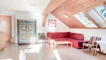 Helles Wohnzimmer im Dachgeschoss mit Holzbalken, gemütlichem Sofa und traditionellem Schrank.