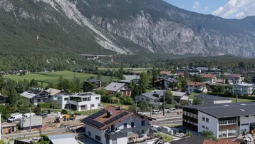 Panoramablick auf eine Wohnsiedlung mit Bergen im Hintergrund und sonnigem Wetter.